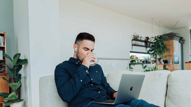 man sitting in a couch, drinking water while using a computer