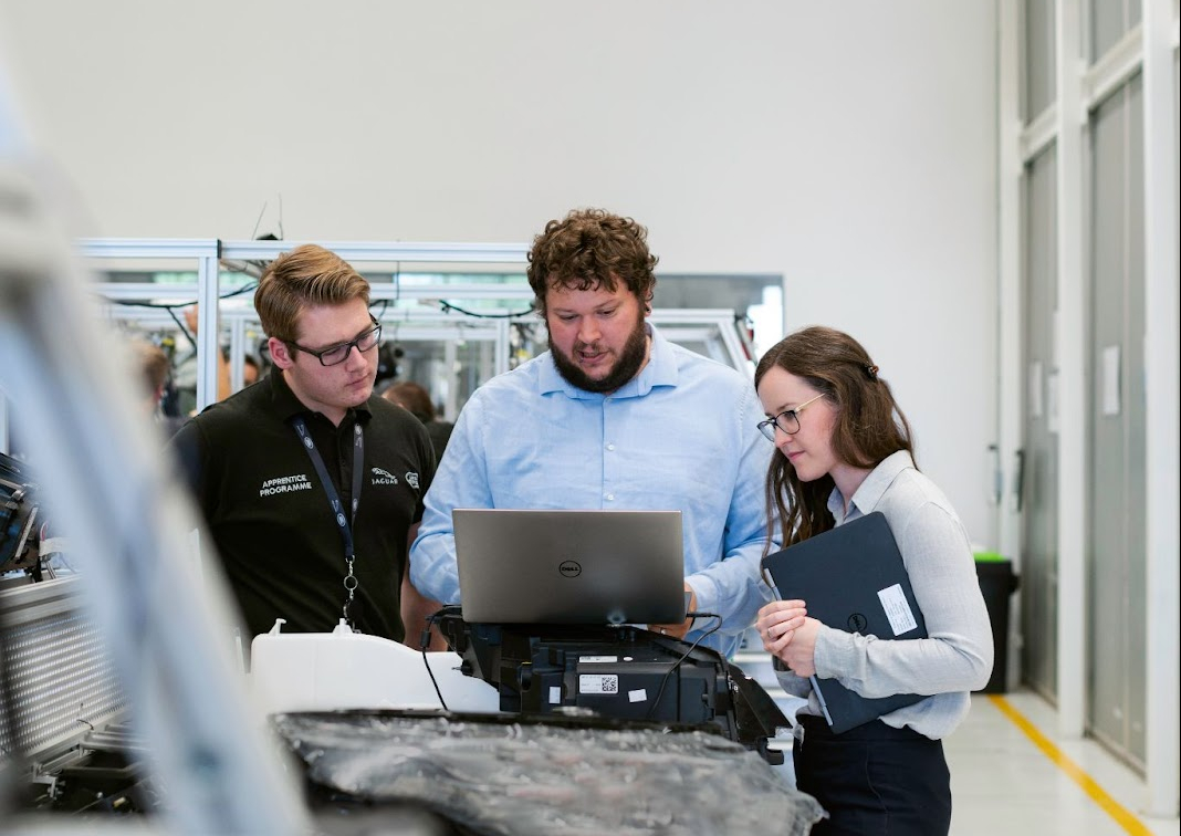 Three people standing around car and tablet