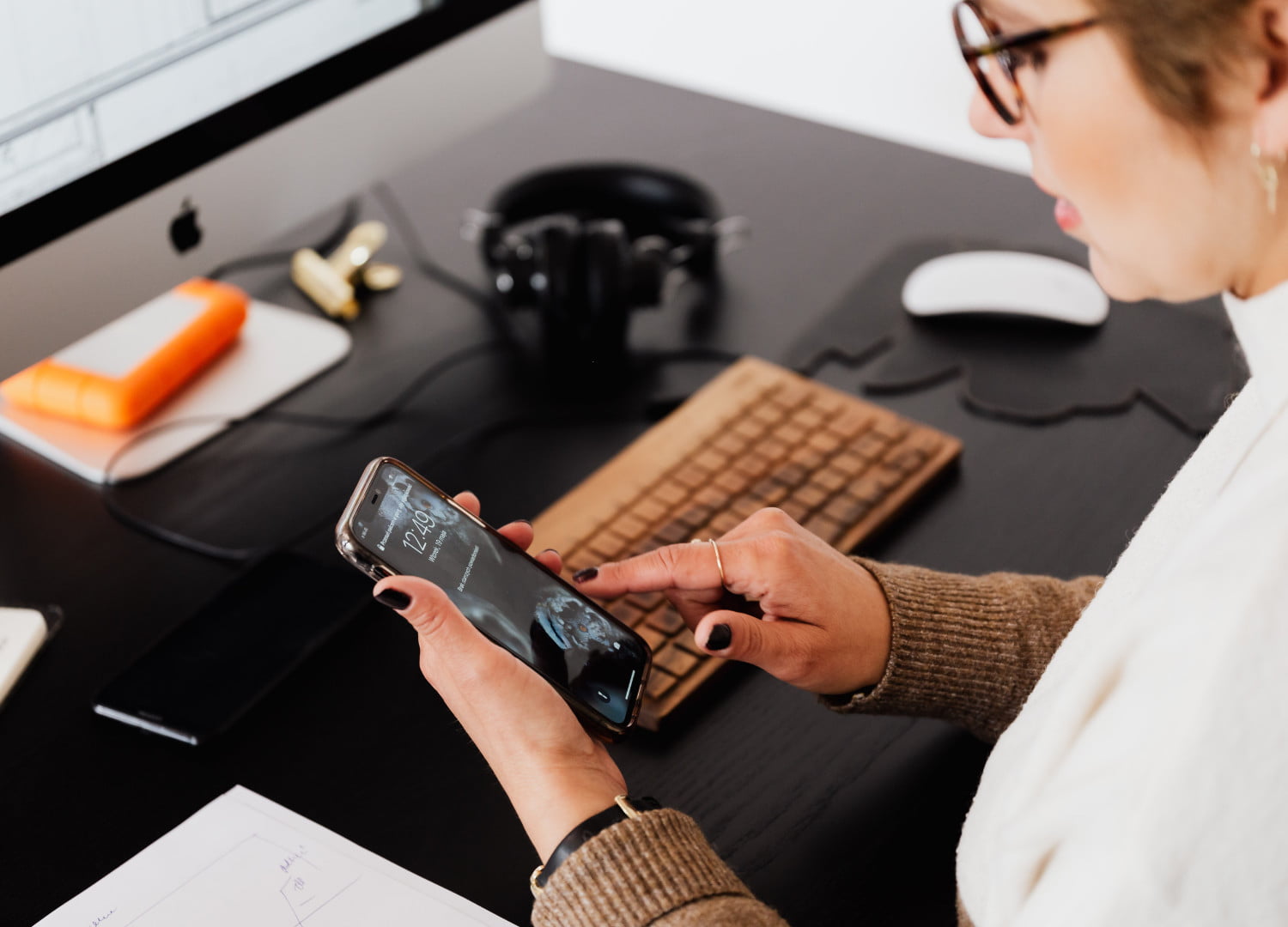 woman sitting in front of computer and looking at her phone