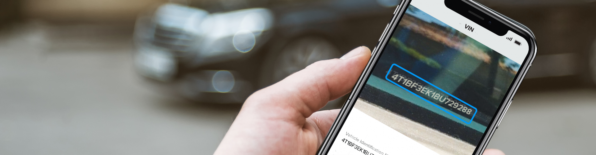 Hand in focus holding a phone with AI-powered VIN scanning technology on the screen with a car in the background